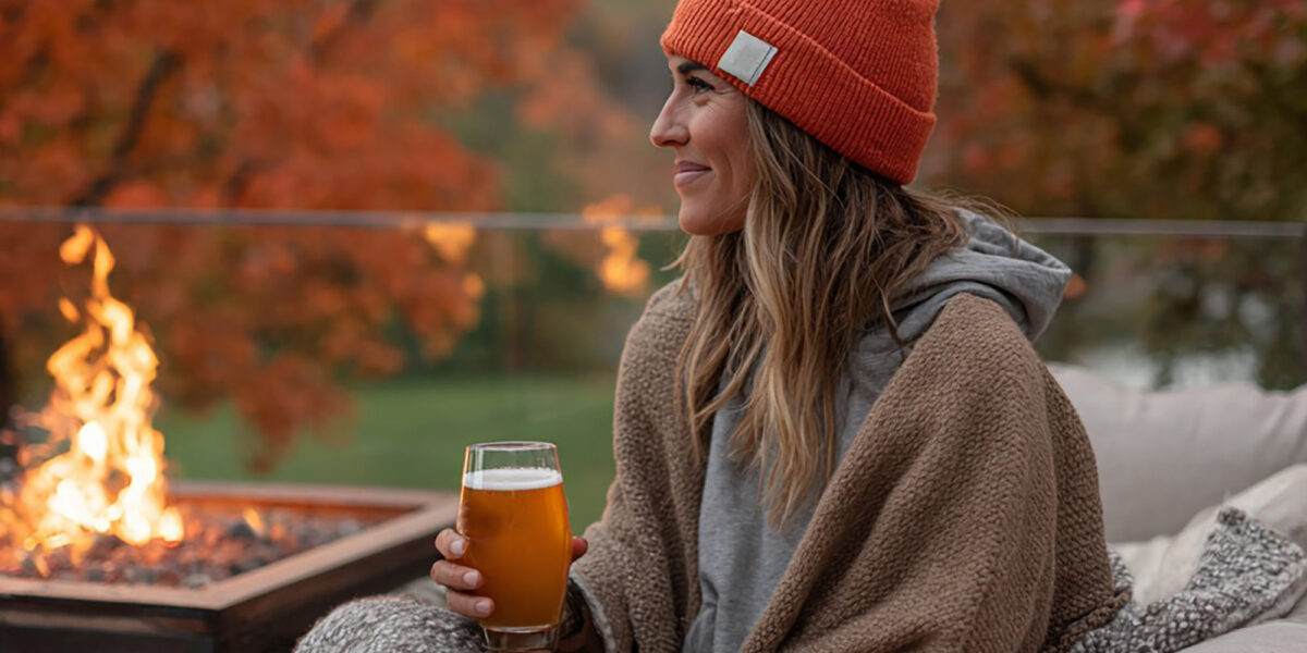 Woman sitting outside enjoying a beer by the fire